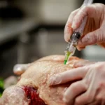 Close-up of a marinade injector being used on raw turkey meat.